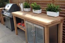 a small outdoor kitchen with a large wooden kitchen island and a drink cooler built-in under the top, a grill next to it is cool