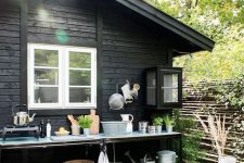 a small outdoor kitchen with open shelves, a small cooker and rustic buckets and baskets for storage, potted herbs