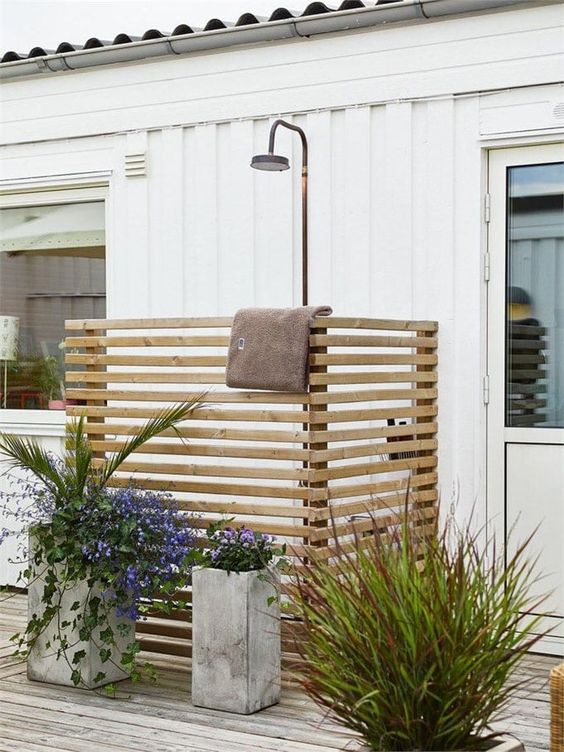 a small outdoor shower space with screens of planked wood, potted plants and blooms is a cool nook to refresh yourself