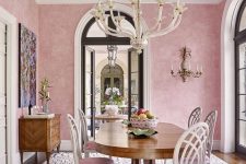a sophisticated dining room with pink wallpaper walls, a decorated slanted ceiling, a vintage dining table and pink chairs plus a printed rug