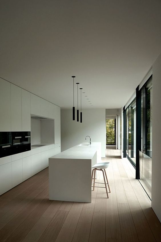 a sophisticated minimalist white kitchen with sleek cabinetry, built-in black appliances and black pendant lamps