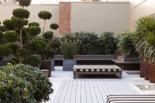 a stylish and elegant rooftop terrace with a neutral wooden deck, cool striped daybeds, lots of potted greenery and trees