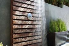 a stylish outdoor shower space with a concrete wall, a wooden planked wall and mate, a crate with stuff and growing plants