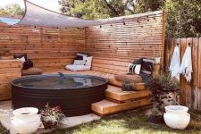 a stylish pool nook with a black stock tank pool, planked screens, wooden ladders and a bench, potted plants and printed pillows