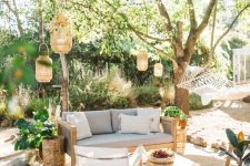 a summer boho patio with a grey sofa, neutral chairs, a low coffee table, lanterns hanging over the space, potted plants