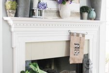 a summer farmhouse mantel with buckets, bright faux blooms and greenery, a lavender wreath, some milk bottles and oversized leaves