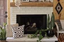 a summer-inspired fireplace with a potted plant, a branch, vintage jugs, some artworks and printed pillows by the fireplace
