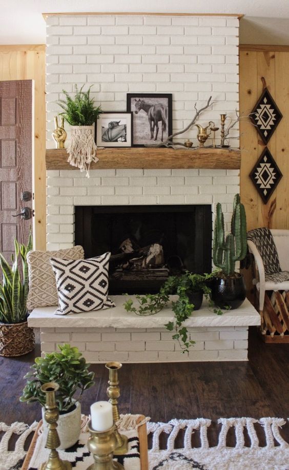 a summer inspired fireplace with a potted plant, a branch, vintage jugs, some artworks and printed pillows by the fireplace