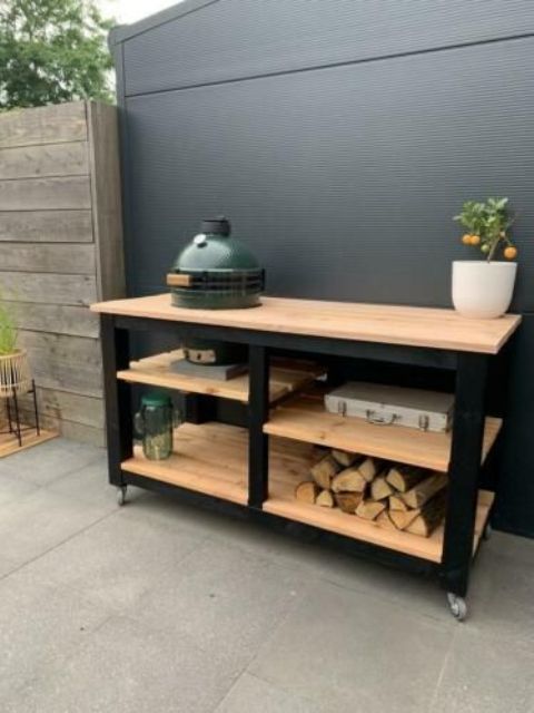 A tiny outdoor kitchen of an open kitchen island with firewood, a grill and various necessary stuff around plus a potted plant
