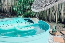 a turquoise stock tank pool with a funny float, with pebbles around and an umbrella is a lovely and pretty space for outside