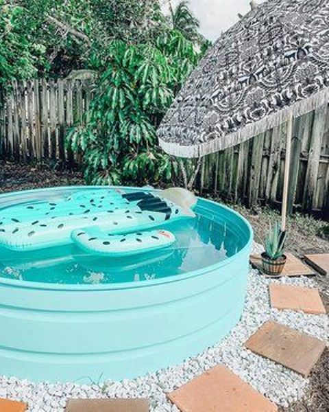 a turquoise stock tank pool with a funny float, with pebbles around and an umbrella is a lovely and pretty space for outside