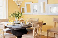 a vintage dining room with yellow walls, a vintage dark stained table, vintage neutral chairs, a crystal chandelier and a ledge with frames