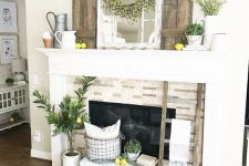 a vintage summer mantel with lemons, greenery in vases and pits, a mirror, a yellow floral wreath and jugs