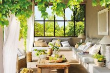 a welcoming Mediterranean terrace with a built-in corner sofa,  a low wooden table, baskets, lanterns and greenery and blooms