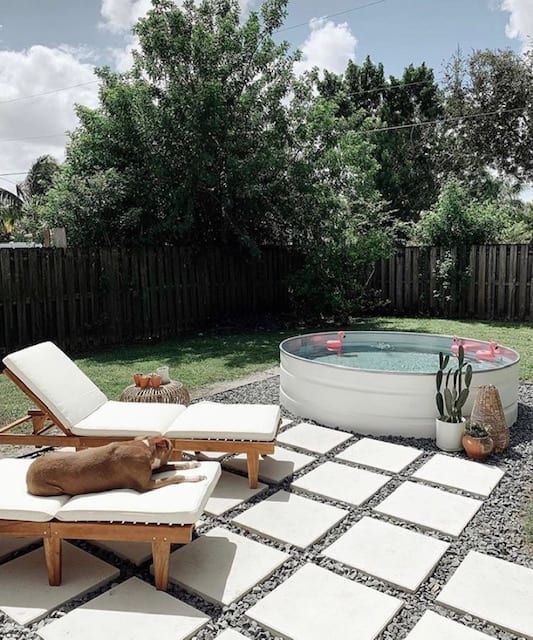 a welcoming backyard with gravel and tiles, loungers, candle lanterns, a white stock tank pool with floats and potted plants