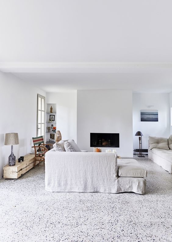 a welcoming living room in white, with a pretty terrazzo floor, a built-in fireplace and ecletic furniture pieces