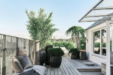 a welcoming rooftop terrace with a wooden deck, modern furniture, cushions and pillows, potted plants and trees