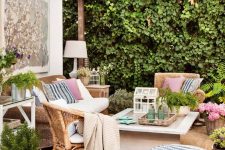 a welcoming summer terrace with woven furniture, a small coffee table, layered rugs, printed pillows and blankets