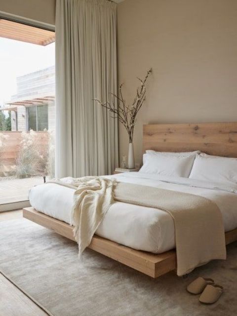 a zen minimalist bedroom with dove grey walls, ligth grene curtains, a stained floating bed and neutral bedding is welcoming
