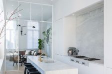 an airy white minimalist kitchen with sleek cabinetry, a kitchen island with a waterfall countertop and black stools