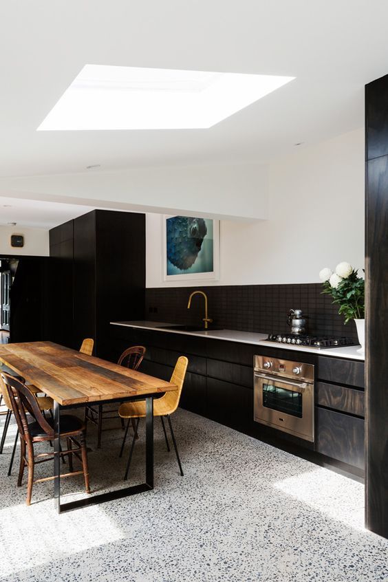 an elegant kitchen with a black and white terrazzo floor, dark stained cabinets, a stained table and woven chairs is lovely