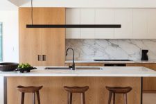 an elegant minimalist kitchen with white and light stained cabinetry, a large kitchen island, a marble backsplash and wooden stools