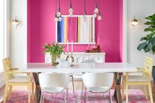 an eye-catchy dining room with a hot pink niche with a bar, a long dining table and mismatching chairs plus bulbs over the space