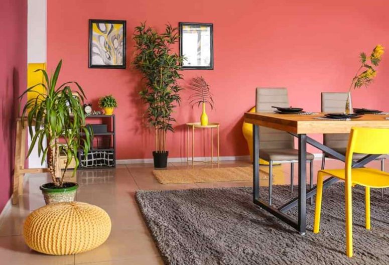 an inspiring bright pink dining room with a purple accent wall, a stained table and grey chairs, potted plants and bright yellow touches