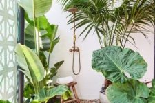 an outdoor tropical shower with pebbles, wooden bath mats, lots of tropical plants and a lovely brass shower is cool