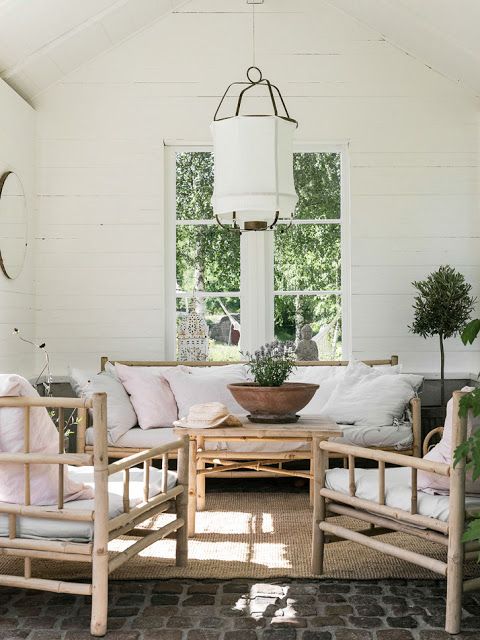 a Nordic veranda with bamboo furniture and neutral and printed textiles, potted greenery and a tree plus a pendant lamp