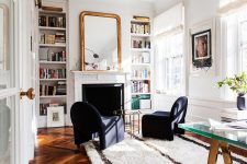 a Parisian chic home office with built-in shelves, a fireplace, navy chairs and a glass table, a glass desk and some art