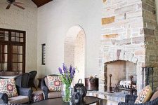 a Provence-inspired outdoor space under a roof with a stone fireplace, black wicker furniture and a black low table, printed textiles