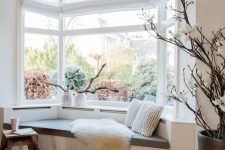 a Scandinavian space with a large bow window and an upholstered daybed by its side plus driftwood arrangements on the windowsill