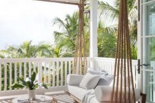 a back porch with a hanging daybed with pillows on multiple ropes, with a chic and delicate coffee table plus potted greenery