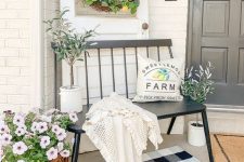 a beautiful farmhouse porch with a black bench, a printed  rug, a lemon wreath and potted plants and blooms is a lovely space to spend some time
