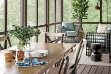a beautiful screened porch with a simple wooden dining set, bold rattan seating furniture, some greenery and lamps is cool