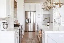 a beautiful white farmhouse kitchen with exposed brick walls, brass pendant lamps, chrome appliances and fixtures is cool