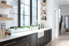 a black farmhouse kitchen with shaker style cabinets and black French windows, open shelves, black and gold sconces and greenery