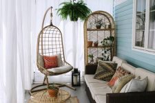 a boho porch with a printed boho rug, a small rattan chair and a big hanging one, a folding table, a wicker sofa and a storage unit