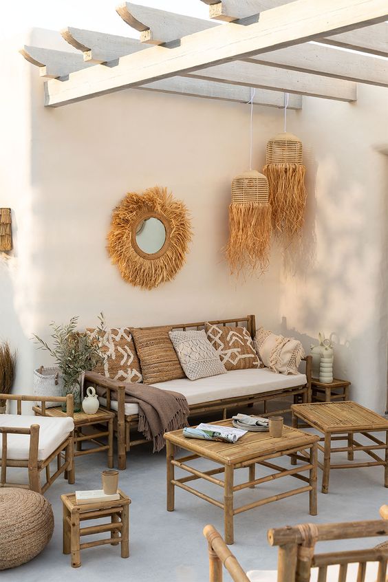 a boho tropical patio with bamboo furniture, neutral and printed textiles, pendant woven lamps, potted greenery is chic