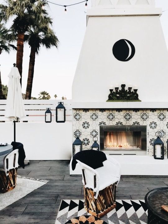 a bold black and white terrace with a lovely fireplace clad with tiles, candle lanterns, printed textiles and rattan chairs is amazing