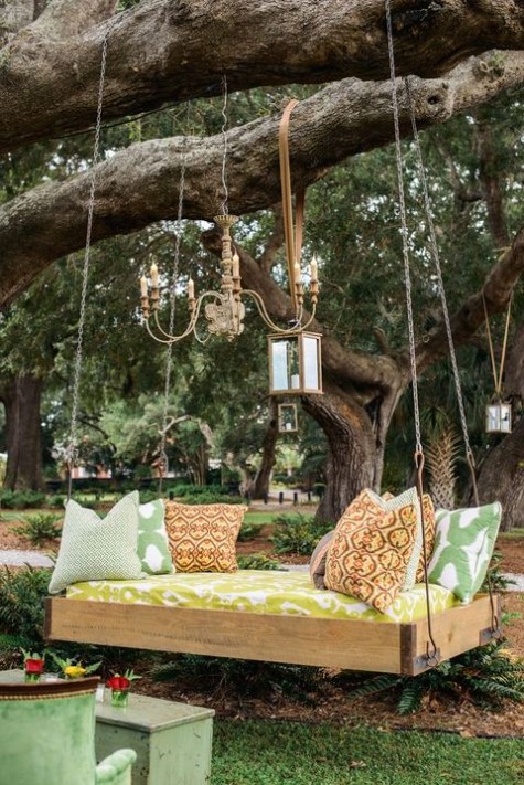 a bold hanging daybed with bright printed pillows and a mattress, with hanging candle lanterns and a chandelier plus green furniture