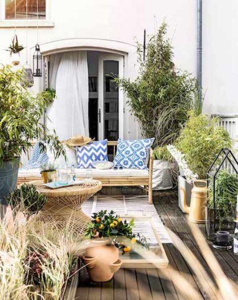 a bright Mediterranean deck with bamboo furniture, blue printed pillows, potted greenery and blooms and lovely terracotta vases