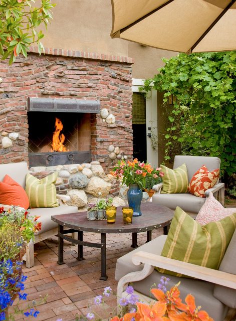 a bright Mediterranean-inspired space with a brick, stone and metal fireplace, neutral furniture with colorful pillows and bold blooms and greenery