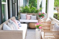 a bright farmhouse porch with light stained rattan, wood and wicker furniture, printed textiles, potted blooms and greenery is a chic and bold summer nook