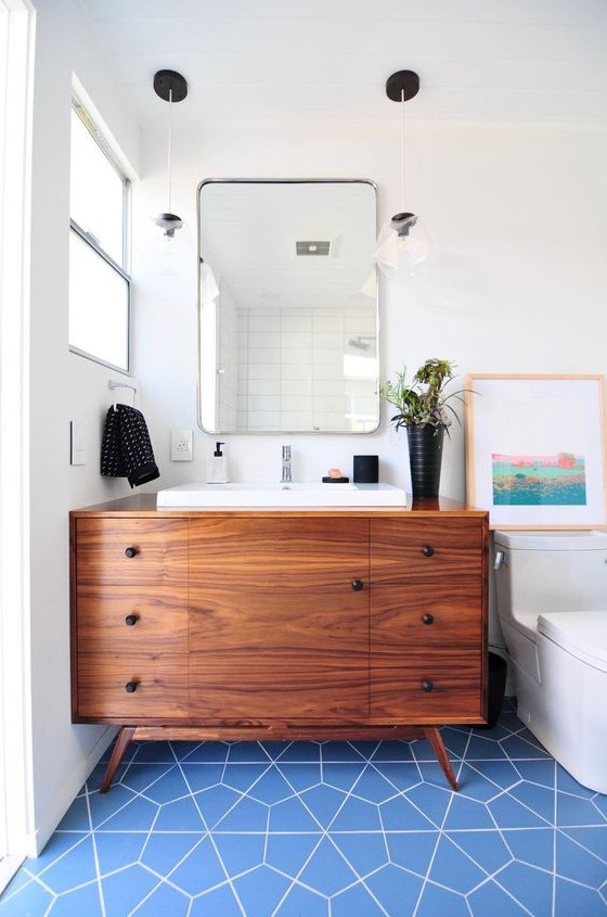 A bright mid century modern bathroom with blue geo tiles on the floor, a rich stained vanity and touches of black for accenting