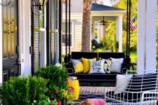 a bright porch with a black hanging daybed, a delicate bench with black and white cushions, potted greenery and blooms