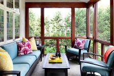 a bright traditional screened porch with black wicker furniture, bright pillows, a low coffee table, bright potted blooms