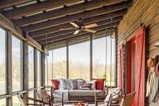a cabin screened porch with rattan and woven furniture, a round coffee table, bright pillows, potted plants and blooms