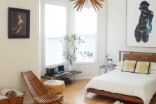 a catchy mid-century modern bedroom with a bay window, stained furniture, a faux animal skin rug, a pretty chandelier and cool art
